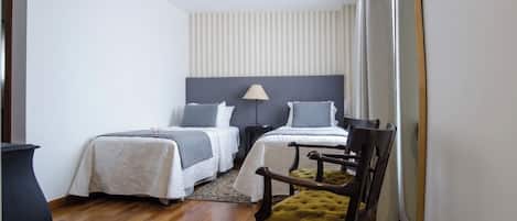 Un dormitorio con dos camas, una mesita de noche, una lámpara, una silla y un espejo grande.