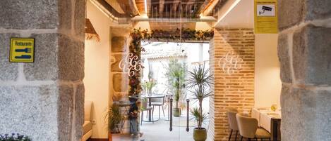 A stone-walled corridor leading to a dining area with a patterned floor, a sign indicating a restaurant, and a security camera on the wall.