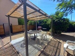 A covered patio with a table and chairs, a wooden bench, and a grill area in the background. - Villa near the beach (La Garde)