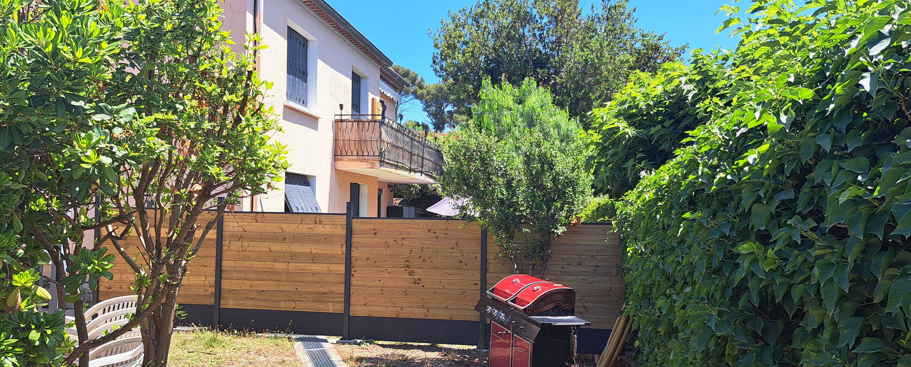Een achtertuin met een houten schutting, een barbecue en een huis met balkon.