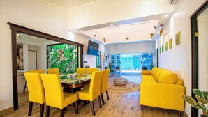 Un soggiorno moderno con un divano giallo, un'area pranzo con sedie gialle e un grande pannello decorativo verde.