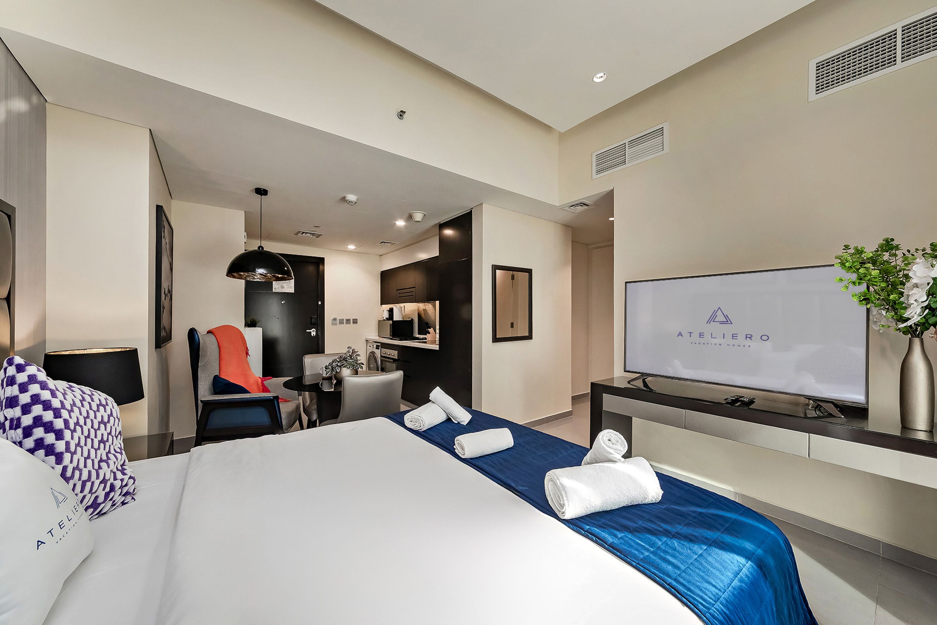 Ett modernt hotellrum med en stor säng, ett skrivbord, en stol, en TV och ett litet pentry.