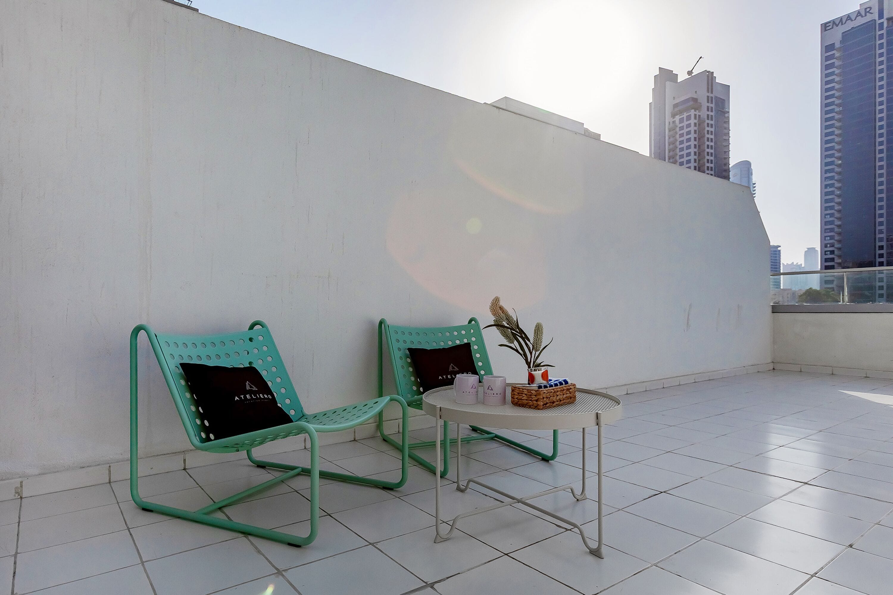 A rooftop terrace with two green chairs, a small table with a plant, and a white wall.
