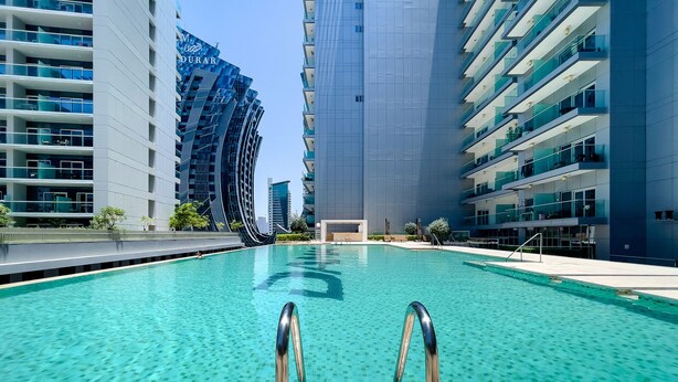 A swimming pool with clear water, surrounded by modern high-rise buildings. - Stylish Studio at DAMAC Majestine (Dubai)