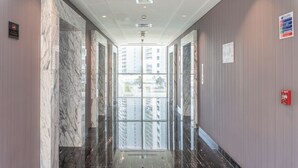 A hallway with marble walls and floors, leading to a glass elevator. - Stylish Studio at DAMAC Majestine (Dubai)