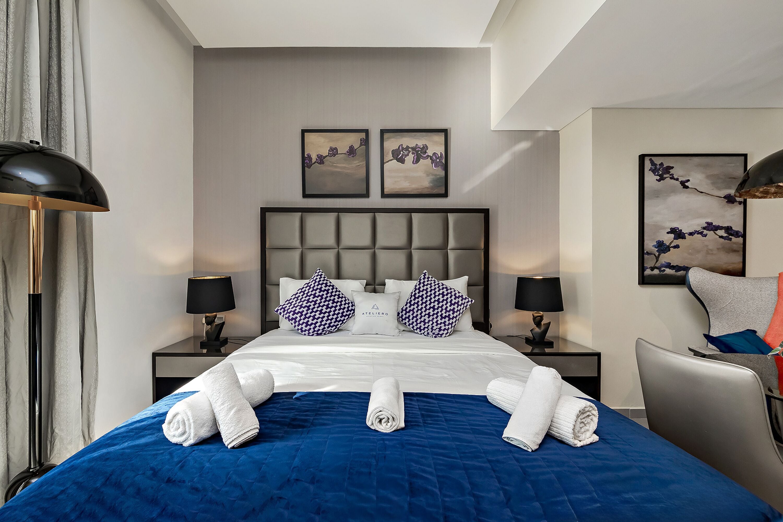 Une chambre d’hôtel avec un grand lit, deux tables de chevet, une chaise et des œuvres d’art accrochées aux murs.