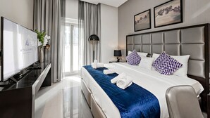 A modern hotel room with a large bed, a flat-screen TV, a desk, and a window with curtains. - Stylish Studio at DAMAC Majestine (Dubai)