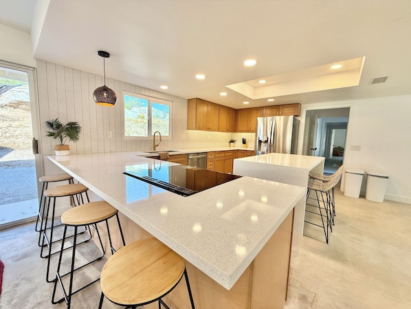 A modern kitchen with a large island, wooden bar stools, and a view of the outdoors.