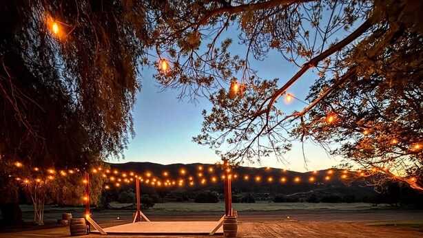 Un espace extérieur aménagé avec des guirlandes lumineuses, un banc en bois et un sol à motifs.