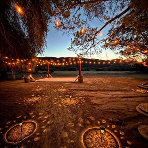 An outdoor seating area with string lights, a wooden bench, and a patterned ground surface. - Golden Valley Ranch is a peaceful retreat with views, nature, and calm. (Hemet)
