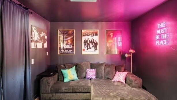 A cozy living room with a sectional sofa, a flat-screen TV, and posters on the wall.