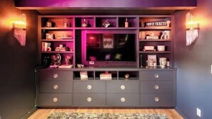 A modern entertainment unit with a flat-screen TV, shelves with various items, and two wall-mounted sconces.