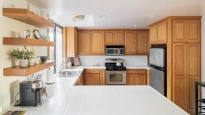 A modern kitchen with wooden cabinets, a stainless steel stove, a microwave, and a refrigerator.