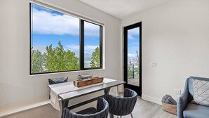 Ein modernes Zimmer mit großem Fenster, einem Tisch, zwei Stühlen und Blick auf Bäume und einen See.