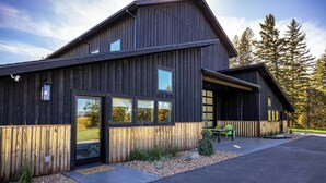 A modern wooden building with large windows, a covered patio, and a gravel driveway. - Paddles Up Private Pickleball Retreat (Whitefish)