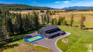 A large building with a tennis court, surrounded by a forest and open fields. - Paddles Up Private Pickleball Retreat (Whitefish)