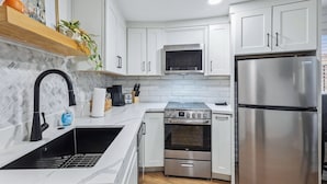 A modern kitchen with white cabinets, a stainless steel refrigerator, a microwave, a stove, and a sink.
