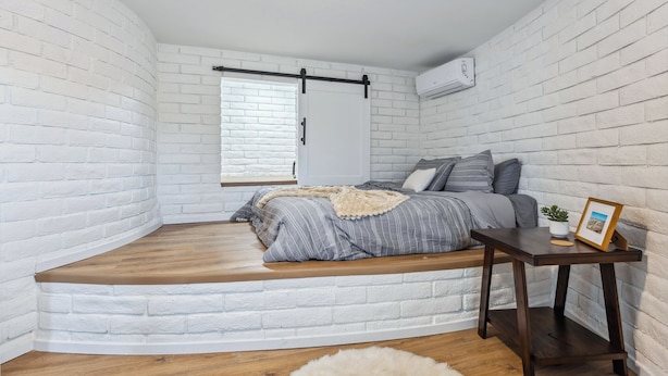 A bedroom with a built-in bench along the curved wall, a bed with gray bedding, a small table with a picture frame, and a window with blinds. - Charming 1-bedroom with stunning Views (Lake Havasu City)