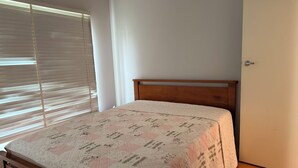 Un dormitorio con una cama de madera, una colcha acolchada, una ventana con persianas y una puerta.