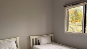 Un dormitorio con dos camas individuales, una ventana que da a árboles y un techo blanco.