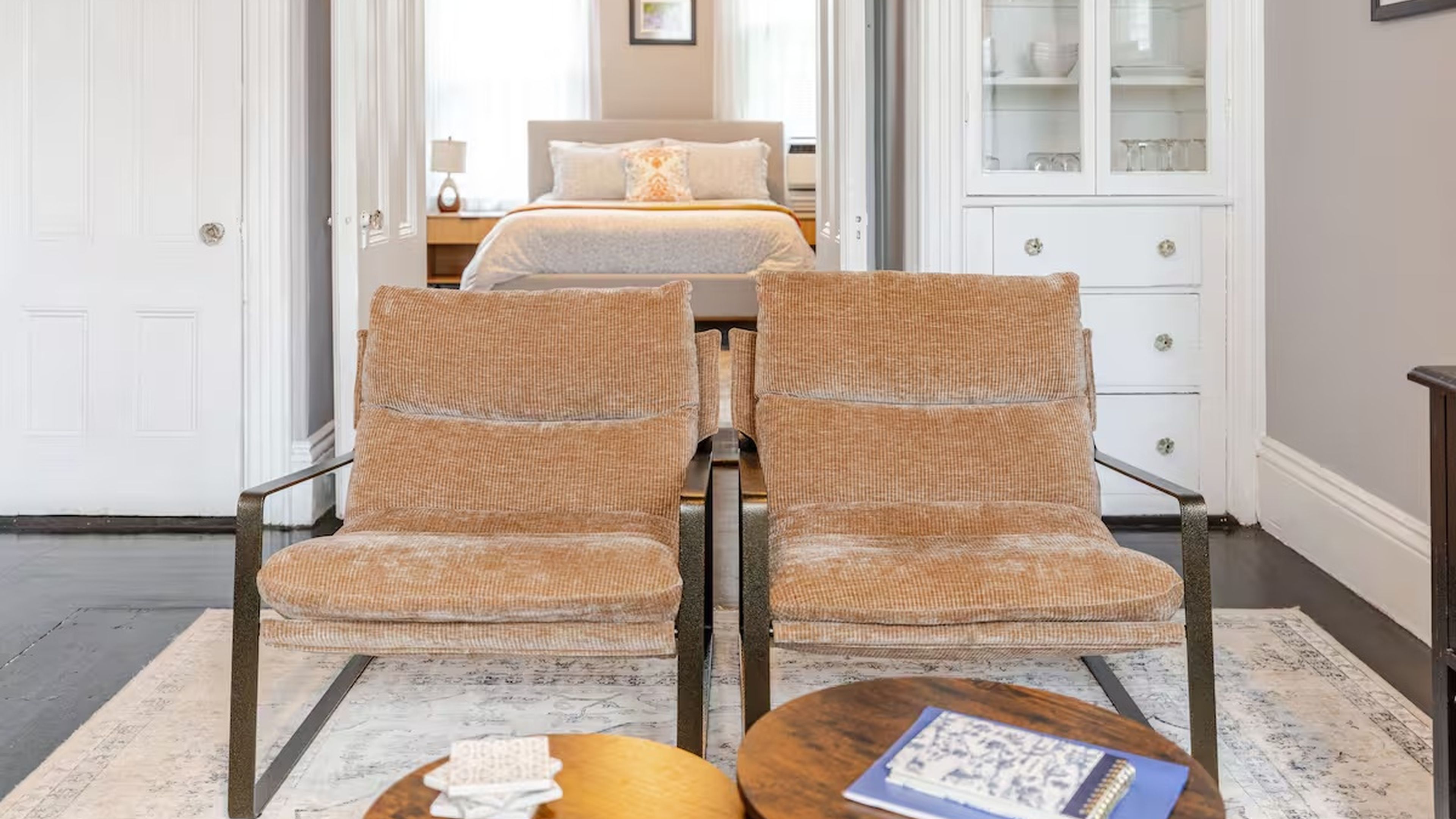 A room with a bed, a white cabinet, and two chairs with a woven texture.