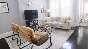 Un salon avec un canapé, un fauteuil, un téléviseur et un ventilateur de plafond.