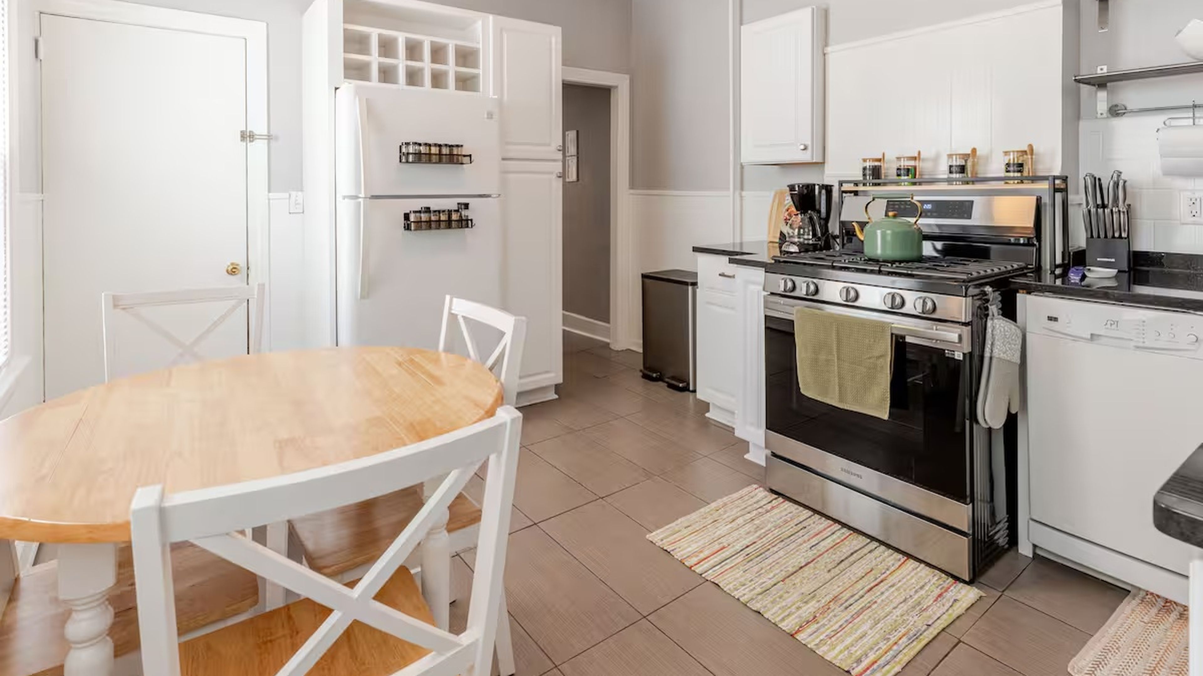A modern kitchen with white cabinetry, a wooden dining table, and stainless steel appliances.