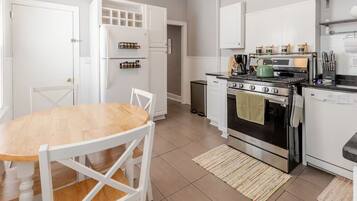 A modern kitchen with white cabinetry, a wooden dining table, and stainless steel appliances.