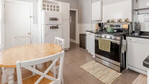 A modern kitchen with white cabinetry, a wooden dining table, and stainless steel appliances. - Charlestown Gem - Historic Neighborhood Steps to Bunker Hill & Boston’s Best (Boston)