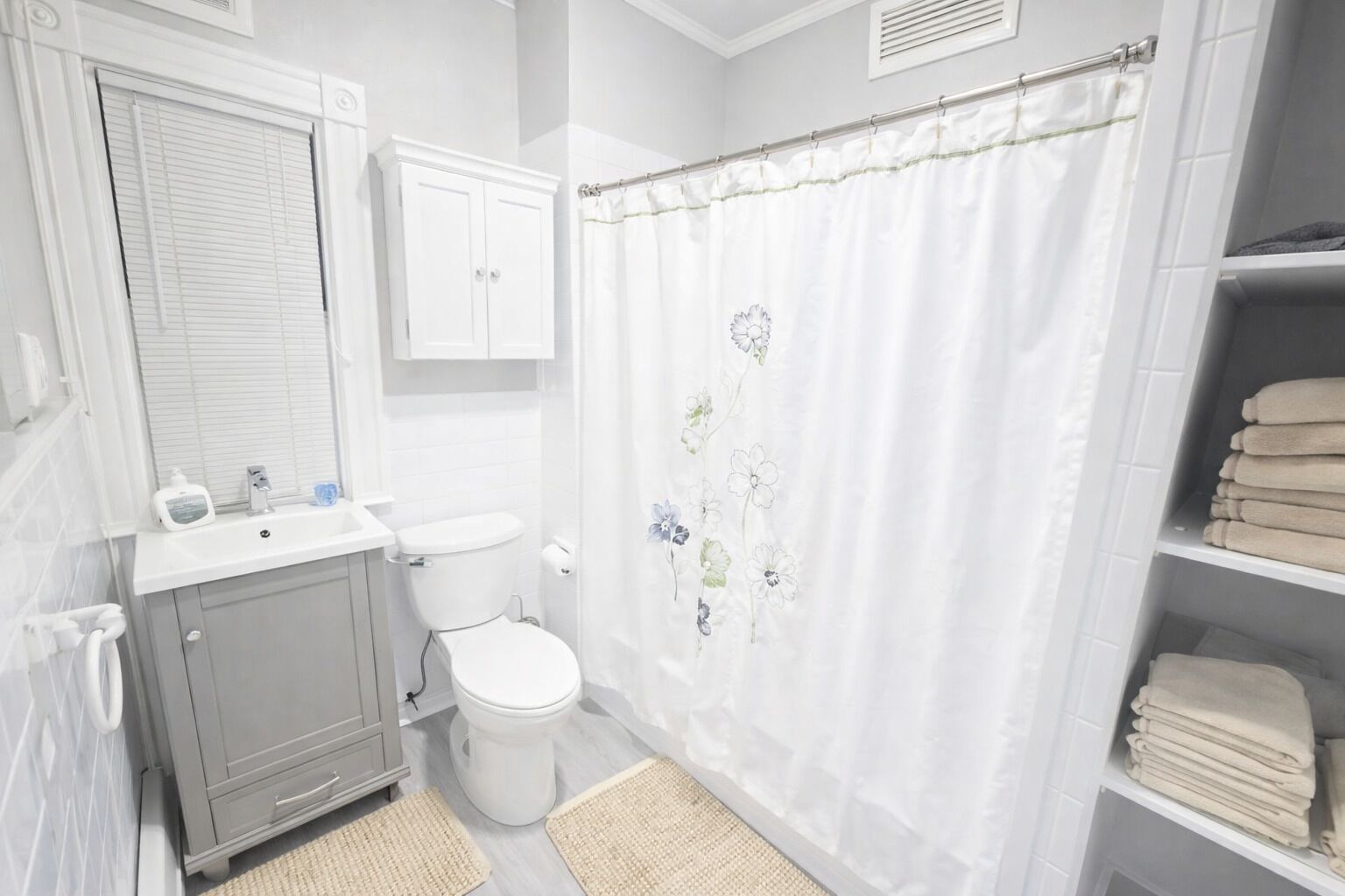 A bathroom with a toilet, sink, cabinet, shower curtain, and a towel rack.