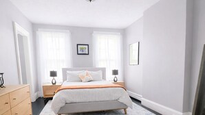 Une chambre à coucher avec un lit, des tables de chevet, une commode et une grande fenêtre.