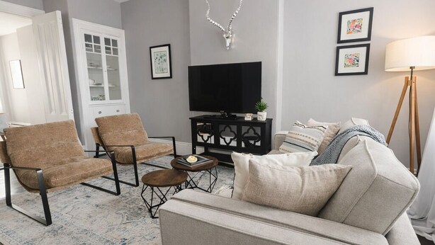 Un salon comprenant un canapé, deux fauteuils, une table basse, un téléviseur, un élément décoratif mural et une lampe sur pied.