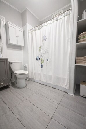 Une salle de bain comprenant des toilettes, un meuble de rangement, un rideau de douche à motifs floraux et une étagère avec des serviettes.