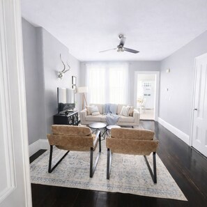 Un salon comprenant un canapé, deux fauteuils, une table basse, un ventilateur de plafond et un tapis.