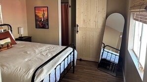 Een slaapkamer met een bed, nachtkastje, schilderij, schuifdeur en een grote spiegel.