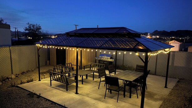 Een overdekt terras met een tafel, stoelen, lichtslingers en een barbecue.