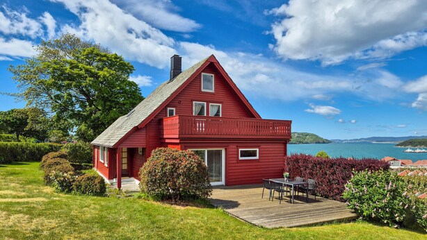 A red house with a deck, surrounded by greenery and a view of the sea. - Awesome home in Fitjar with WiFi (Fitjar)