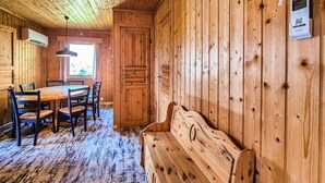 Interno di una baita in legno con un tavolo da pranzo, sedie, una panca e un termostato al muro.