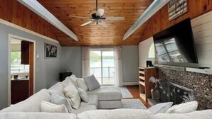 Un salon moderne avec un grand canapé d’angle, un ventilateur de plafond et une cheminée.