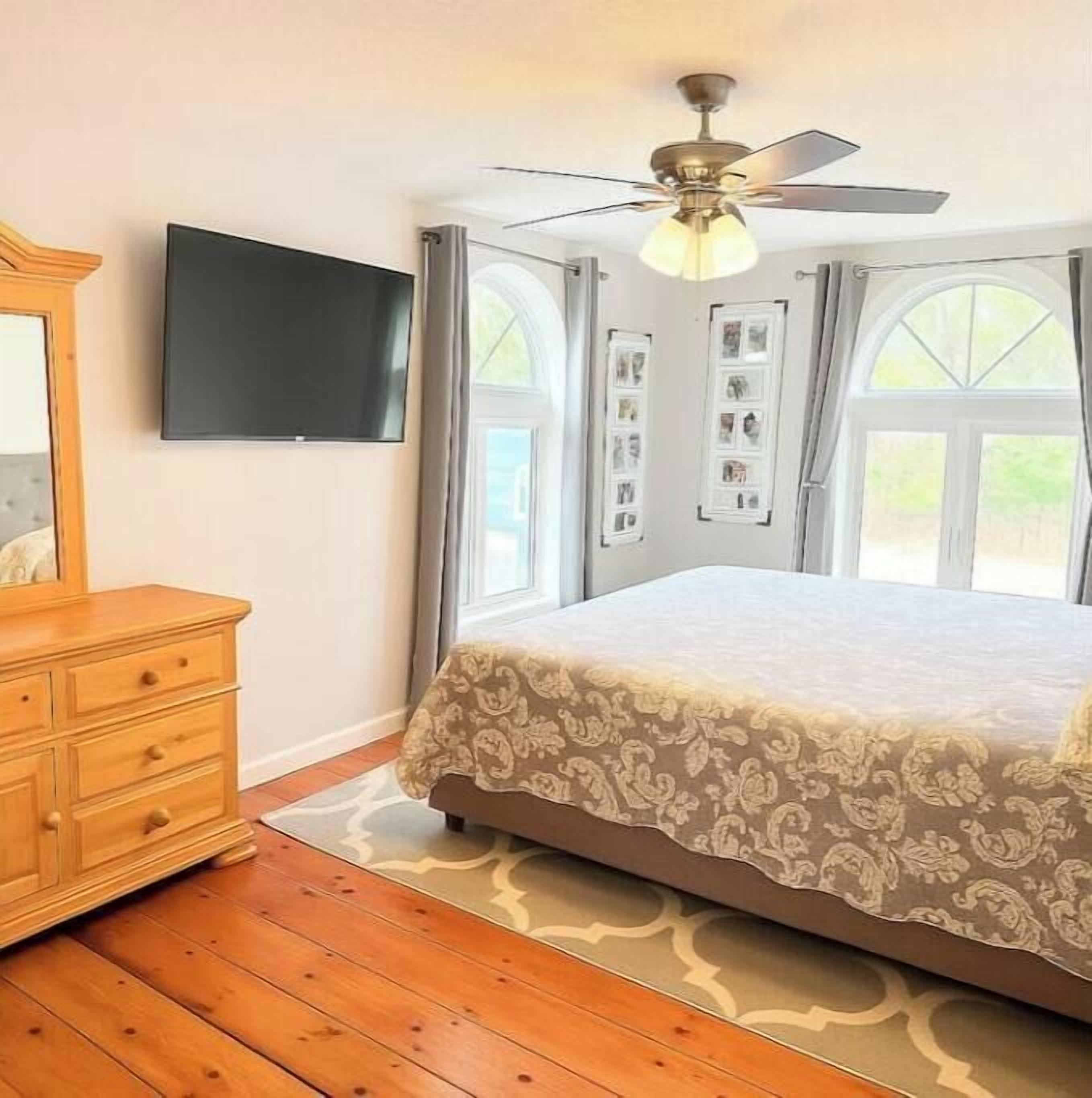 Ein Schlafzimmer mit einem Bett, einem Schminktisch, einem Deckenventilator und einem an der Wand montierten Fernseher.