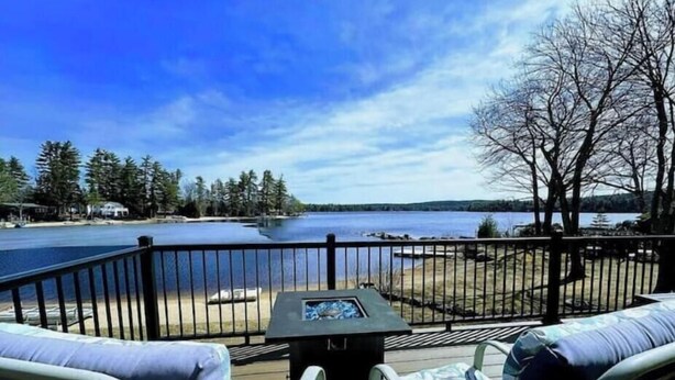 Une terrasse dotée de deux chaises longues et d’une table, offrant une vue sur un lac bordé d’arbres et sur une rive éloignée.