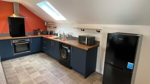 A modern kitchen with a built-in oven, microwave, and refrigerator, a washing machine, and a skylight.
