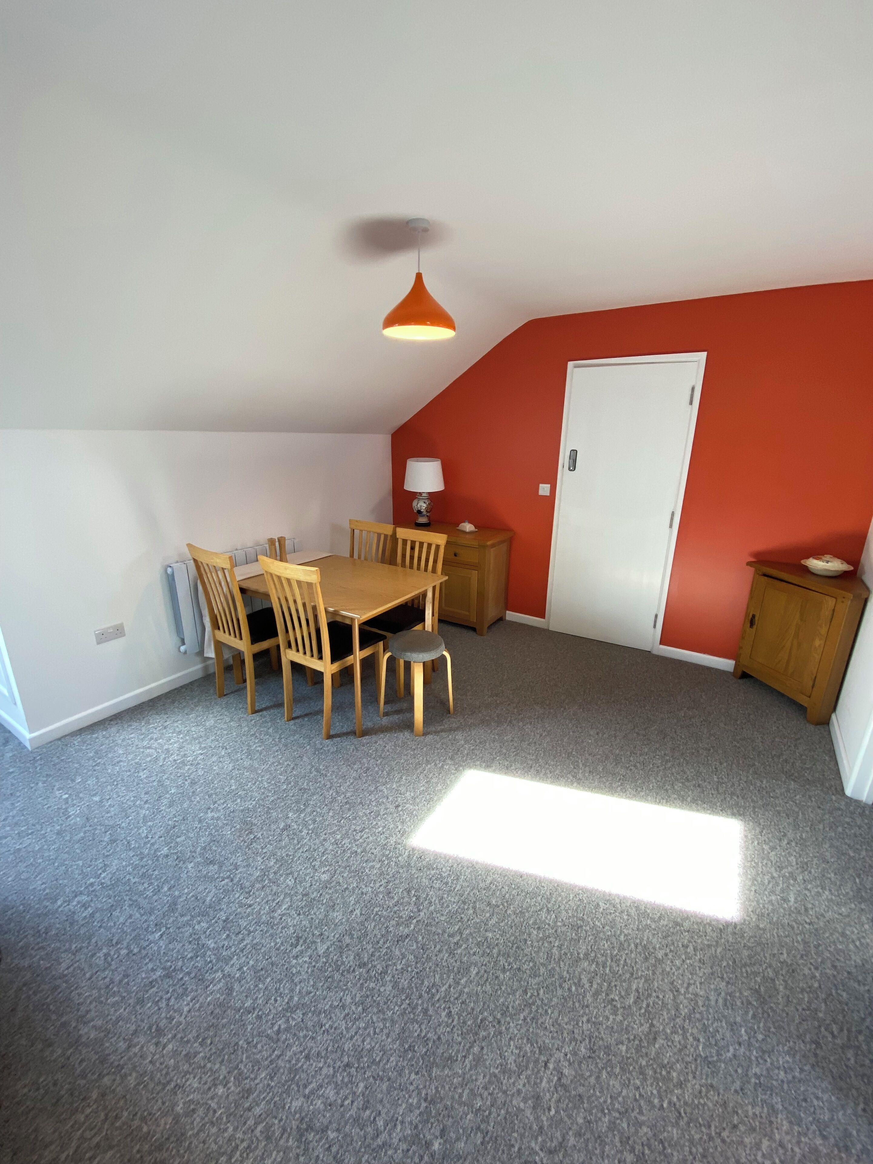 A room with a dining table, chairs, a lamp, a cabinet, and a door.