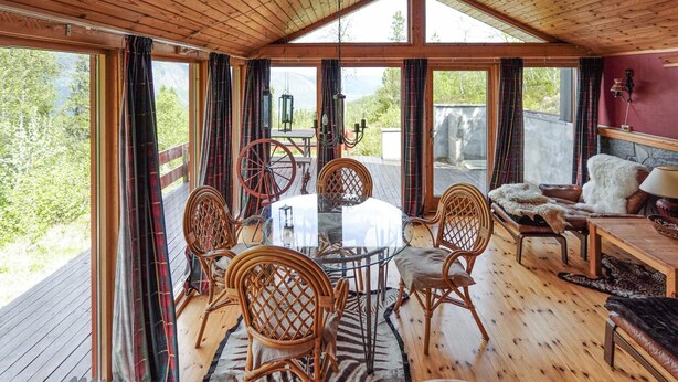 A wooden cabin with a dining area featuring a round table and wicker chairs, a sofa, and a view of the outdoors. - Awesome home in Uvdal with sauna (Uvdal)