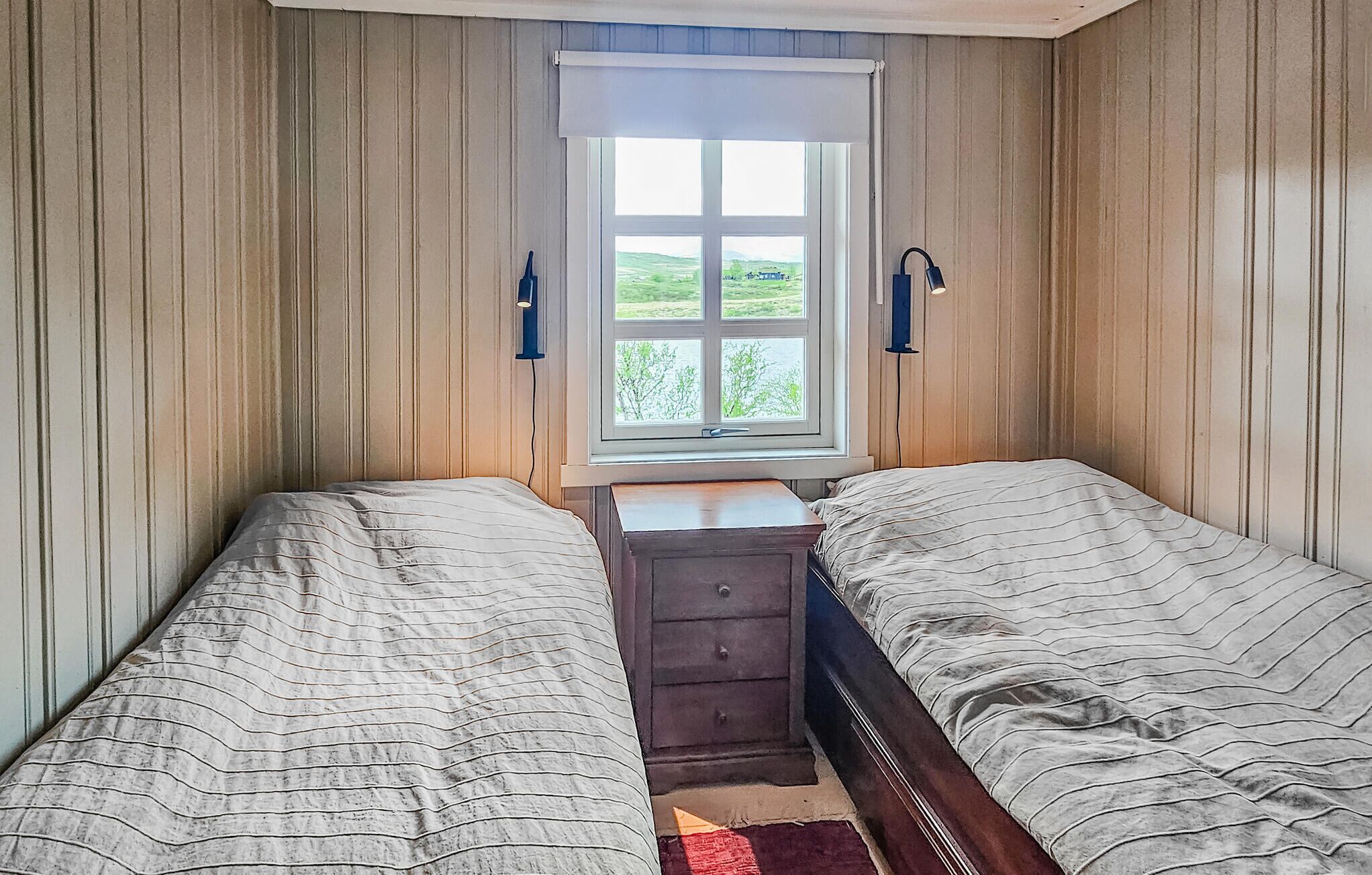 Une chambre avec deux lits simples, une petite commode et une fenêtre donnant sur un espace verdoyant.
