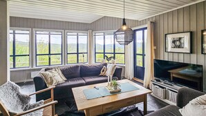 A cozy living room with a sofa, a wooden coffee table, and a television. Large windows offer a view of greenery outside. - Amazing home in Edland with sauna (Edland)