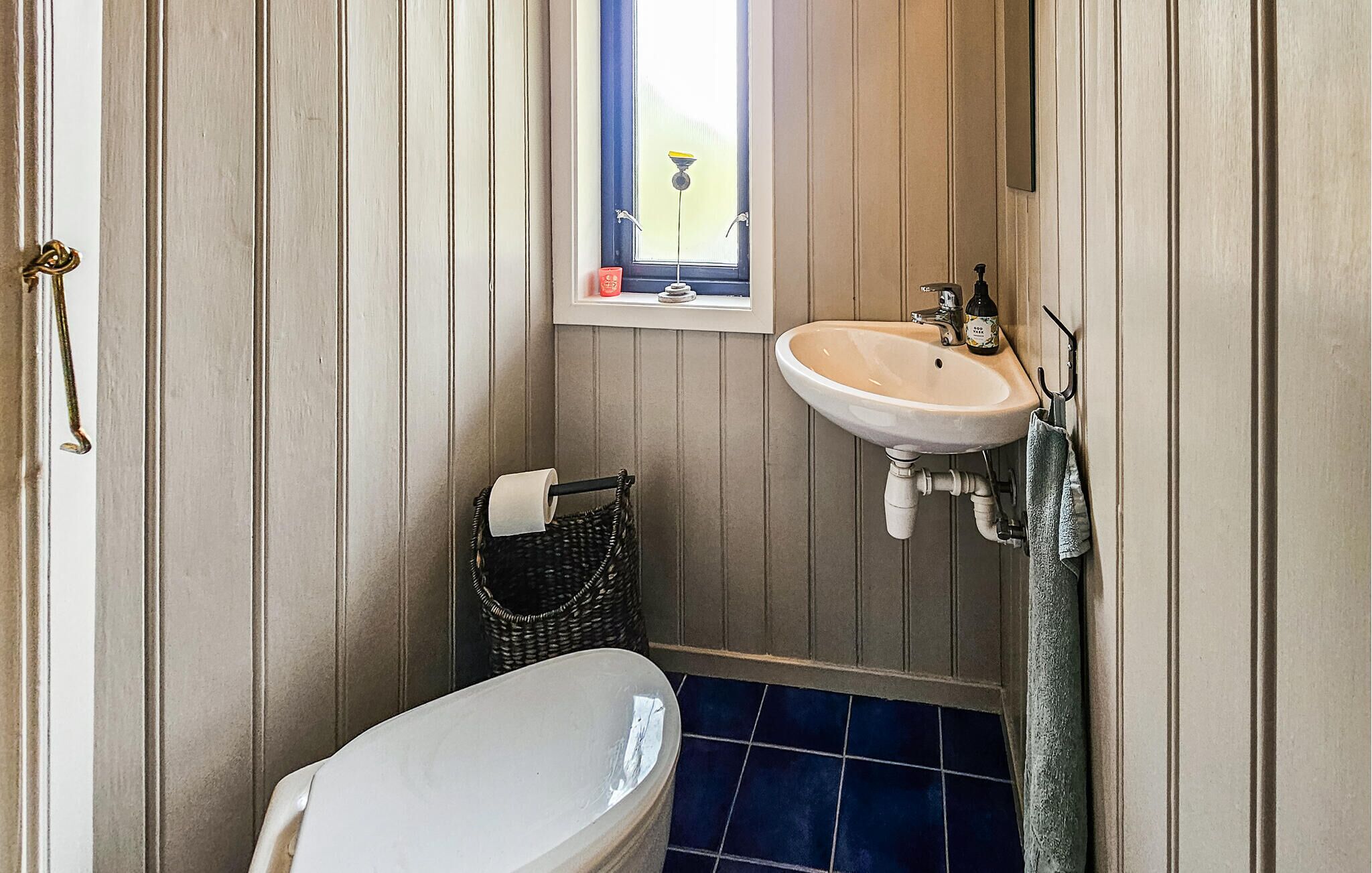 Een kleine badkamer met een wit toilet, een wastafel met spiegel en een raam boven de wastafel.
