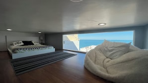 Een slaapkamer met een bed, een groot raam en uitzicht op zee.