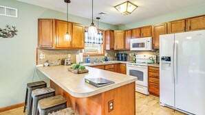 A kitchen with wooden cabinets, a central island, bar stools, a microwave, a refrigerator, and a sink. - Game Room + Lake Access: Albrightsville Escape (Albrightsville)