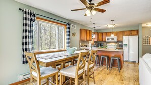 A kitchen with wooden cabinets, a dining table with chairs, a ceiling fan, and a window with curtains. - Game Room + Lake Access: Albrightsville Escape (Albrightsville)